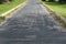 a weathered asphalt path with signs of wear and patchwork, and overgrown grass