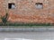 Weathered brick wall with worn windows, sidewalk with weeds and an asphalt road.