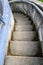 Weathered outdoor concrete stairs curving down into an unknown destination, blue wall and metal handrail