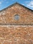 Weathered red brick gable wall with boarded up round window