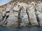 Weathered seaside rock face texture with parts of green and blue water. Aged volcanic stone wall surface background