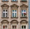 Weathered and stained house facade with rows of windows and one vibrant bunch of flowers on a window sill in Wroclaw, full-frame