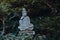 A weathered stone statue of a Buddha or Buddhist monk sitting and observing world, meditates under green trees in japanese garden