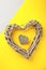 Weaved wooden heart on yellow and grey background. Colour trend 2021