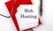 WEB HOSTING text on sticker on red notebook with pen and glasses