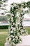 Wedding arches decorated with white flowers and green branches stand on a wooden platform