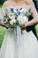 Wedding bouquet of peonies, blue flowers and greenery in bride`s hands