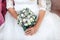 Wedding bouquet of white and purple roses in the hands of brides, close-up, on a white dress background