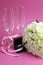 Wedding bridal bouquet of white roses on pink background with pair of champagne flute glasses - vertical.