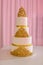 Wedding cake, on white table. 3-tiers covered in ivory fondant sprayed with pearl spray. wedding cake with gold