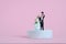 Wedding celebration concept miniature people, toys photography. Bride and groom standing above podium platform isolated on pink