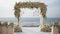 Wedding ceremonial arch decorated with white flowers, sea background. AI generated.