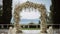 Wedding ceremonial arch decorated with white flowers, sea background. AI generated.