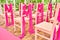 Wedding chairs on each side of archway. Place for wedding ceremony decorated in pink color, wooden chairs for guests outdoors.
