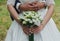 Wedding couple is hugging in the green forest. Bride in satin lace dress with train and tulle veil is holding a bouquet. Bright