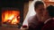 Wedding couple in love warming up in red sweaters by the fireplace. Bride and groom relax and kiss by warm fire and