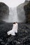 Wedding couple near Skogafoss waterfall. The bride and groom covered with a woolen blanket, where hugging. Snow is
