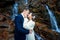 Wedding couple softly hugs on the waterfall. Misty day in mountains