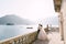 A wedding couple stands on a large terrace with stone columns and statues of lions, overlooking the Bay of Kotor and the