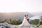 A wedding couple stands on top of a mountain with panoramic views of the Bay of Kotor, at sunset. The groom gently hugs