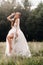 On the wedding day, an Elegant bride in a white long dress and gloves with a bouquet in her hands stands in a clearing enjoying