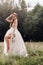 On the wedding day, an Elegant bride in a white long dress and gloves with a bouquet in her hands stands in a clearing enjoying