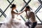 On the wedding day, a handsome groom kneeling kisses his wife hand against the backdrop of a designer window