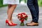 Wedding details: stylish red and brown shoes of bride and groom. Bouquet of roses standing on the ground between them. Newlyweds s