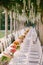 Wedding dinner table reception. A very long table for guests with a white tablecloth, floral arrangements, glass plastic