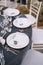 Wedding dinner table reception. White round plates on a round table with gray tablecloth, white Chiavari chairs with