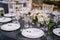 Wedding dinner table reception. White round plates on a round table with gray tablecloth, white Chiavari chairs with