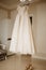 Wedding dress on hanger and shoes on the floor in the bride room. On her wedding day