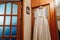 A wedding dress hanging in a doorway in a room on a brown background. Family, marriage, holiday, celebration, wedding