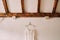 Wedding dress hangs on a hanger on a white wall under wooden ceiling beams