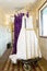 Wedding dress and purple bridrsmaid dresses hanging on a bell cart