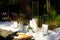 Wedding party banquet outdoors in pine forest. Dining tables decorated in boho style with candles in glass vases, white