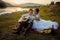 Wedding picnic composition on the river bank during the sunset. Smiling groom is playing the guitar while bride is