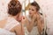 Wedding preparation. Beautiful young bride in white wedding dress indoors. Luxuty model looking at mirror and put on earring, at h