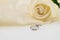 Wedding ring and white rose on ivory silk satin