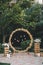 Wedding round arch in rustic style decorated with grass hay field color and retro light bulbs. Near the wooden boxes