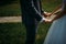 Wedding theme, holding hands newlyweds on green grass background. Hands of the bride and groom close-up. A couple on their wedding