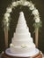 Wedding Theme, Very large multi-tiered completely white only wedding cake under an golden arch with white roses and green leaves