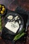 Wedge of Roquefort cheese in a steel plate with olives and herbs. Dark background. Top view