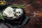 Wedge of Roquefort cheese in a steel plate with olives and herbs. Dark background. Top view. Copy space
