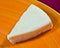 A wedge of soft camembert cheese on an orange plate.