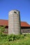 Weeds and foliage grow around an old silo and barn