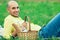 Weekend picnic concept. Portrait of a young handsome bald man in trendy clothes lying on green grass in the park. Picnic basket