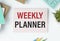 WEEKLY PLANNER on notepad. Business concept with office tools on chart background