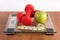 Weight scale with red dumbbell, measuring tape and fresh green apple on wooden floor