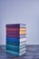 A weighty stack of bright smart books in textural fabric multi-colored covers on an old wooden table on a light background.